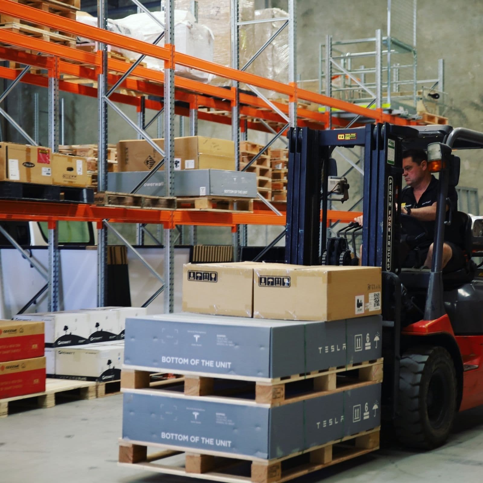Mark moving palletised Tesla Powerwall units by forklift through the Bibra Lake warehouse.