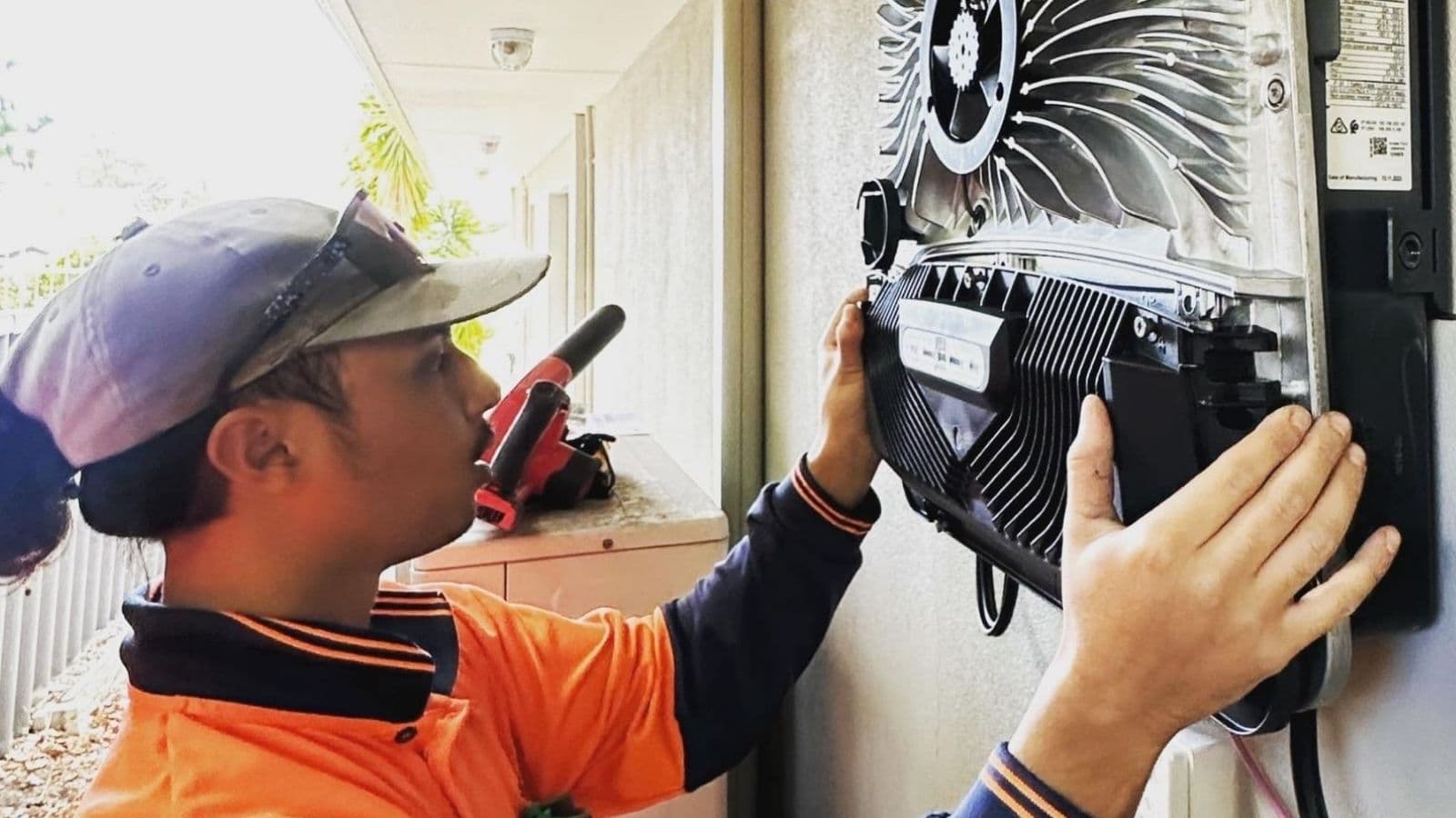 An apprentice fitting the cover onto a wall-mounted inverter